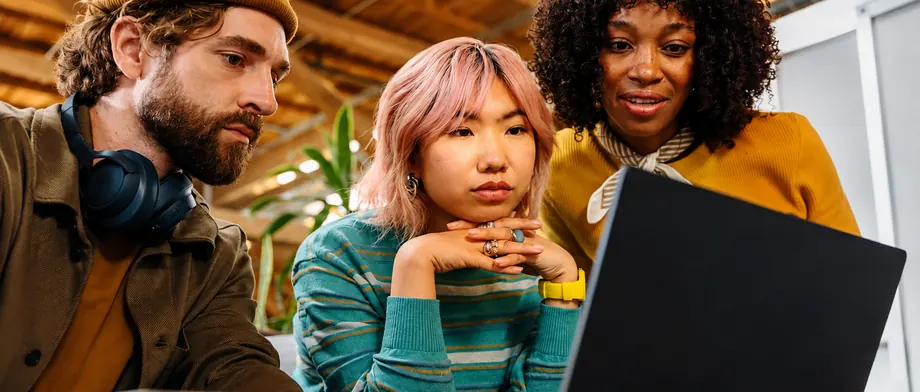 Three colleagues looking at a laptop screen together